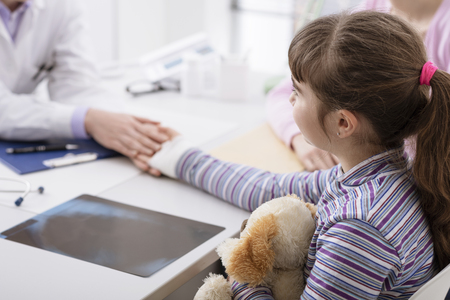 Young girl with fractured wrist in the doctor's office, the pediatrist is checking her bandage and visiting her, kids and healthcare conceptの写真素材