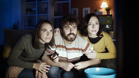 Friends sitting on the sofa at home and watching suspense movies togetherの写真素材