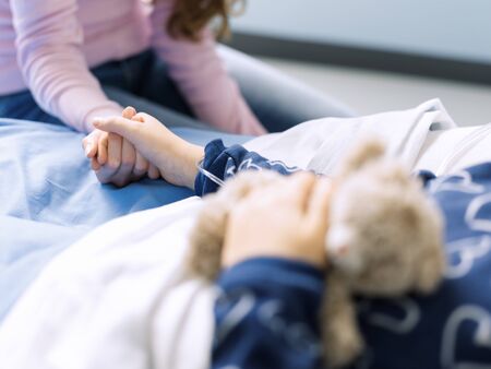 Loving young mother assisting her daughter on the hospital bed, they are holding handsの写真素材