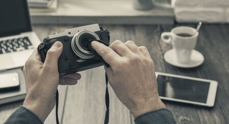 Hipster photographer at home sitting at desk and cleaning his camera lens with a cloth, point of...