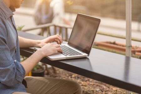 Unrecognizable man using a modern portable computer on an outdoor table, street on background