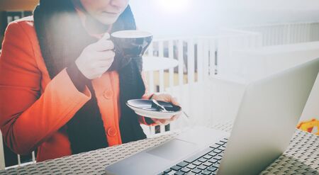 Woman drinking a cappuccino at the cafe and working on her laptop on a open air terraceの写真素材