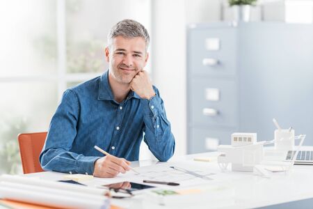 Professional architect sitting at office desk and working, he is checking a project blueprint, engineering and architecture conceptの写真素材