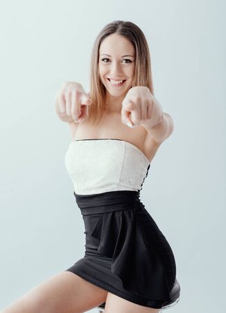 Elegant young girl pointing at camera and smiling, she is sitting on a stool and posingの写真素材