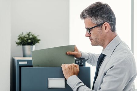 Businessperson at work: professional confident office clerk searching files in the filing cabinet