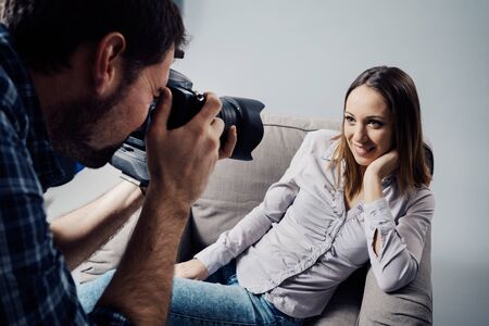 Professional photo shoot at the studio, a female model is posing on an armchair and smiling; the...