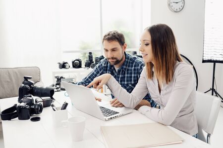 Photographer and designer in a creative agency, they are sitting at desk and working together with a laptopの写真素材