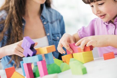 Young mother and child playing together at home with colorful toy wood blocks, family and leisure conceptの写真素材
