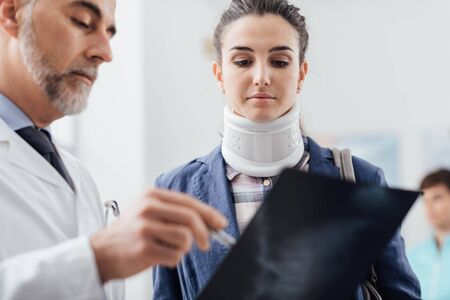 Doctor examining a young female patient's x-ray, she is wearing a cervical collar and having a serious spinal injuryの写真素材