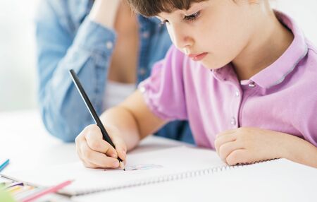 Mother and child spending time together at home, the girl is drawing on a notebook with a pencilの写真素材