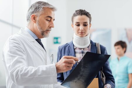 Doctor examining a young female patient's x-ray, she is wearing a cervical collar and having a serious neck injuryの写真素材