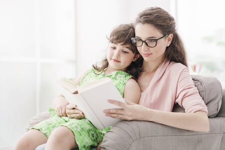 Young mother and child relaxing at home in the living room, they are sitting on the armchair and...