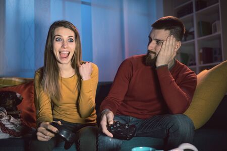 Happy couple playing video games at home, the girl won and is celebrating with fist raisedの写真素材