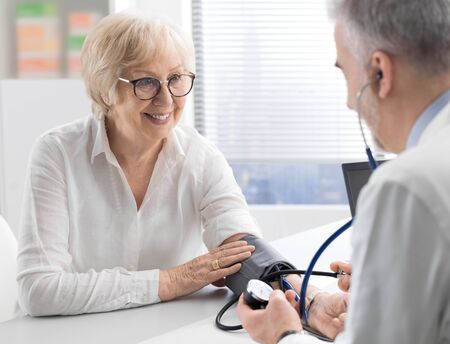 Professional doctor visiting a senior patient and measuring blood pressure using a sphygmomanometer,...