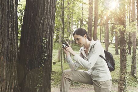 Young woman walking in nature and taking pictures outdoors with her digital camera, hobby and...