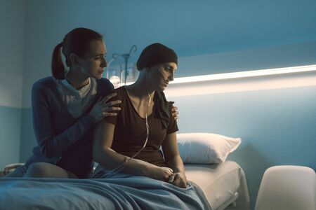 Caring woman assisting her sick friend with cancer at the hospital, she is comforting her