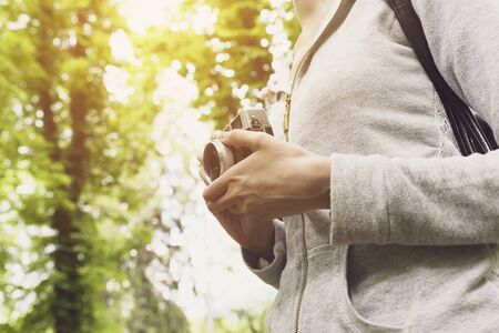 Young woman walking in nature and taking pictures, she is holding her digital camera, hands close upの写真素材
