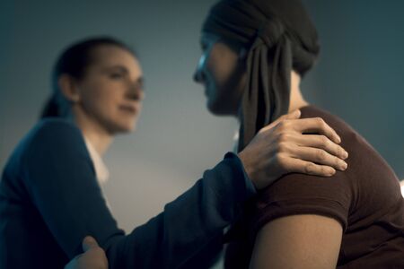 Caring friend supporting and comforting her sick friend with cancer, friendship and assistance conceptの写真素材