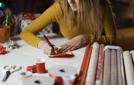 Young woman preparing Christmas gifts and writing wishes on a card: holidays and celebrations...