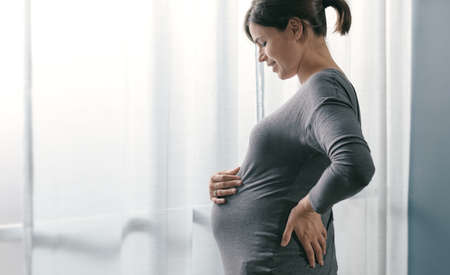 Happy pregnant woman at home, she is standing and touching her belly, pregnancy and motherhood...