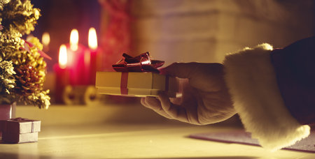 Santa Claus bringing a beautiful gift during Christmas eve's night, hand close up, lit candles on...