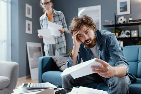Desperate man checking household bills, his wife is looking at him in the background, househould...