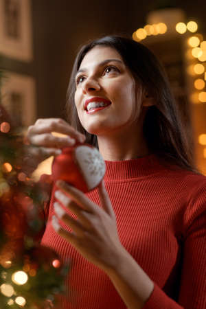 Happy woman hanging a Christmas ball on the tree, holidays and celebration concept