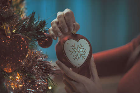 Woman decorating her Christmas tree at home, she is hanging a beautiful bauble