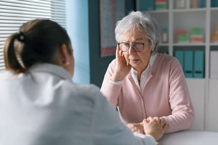Caring doctor assisting a senior patient in her office, she is comforting herの写真素材