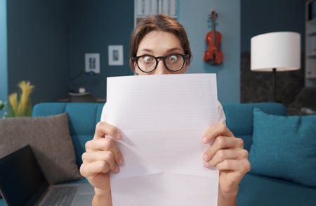 Shocked woman holding a sheet and staring with eyes wide open, expensive bills and debt concept