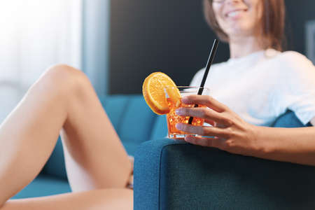 Happy young woman relaxing at home, she is sitting on the couch and having a drink