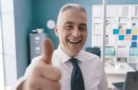 Cheerful executive celebrating his success in his office and giving a thumbs up