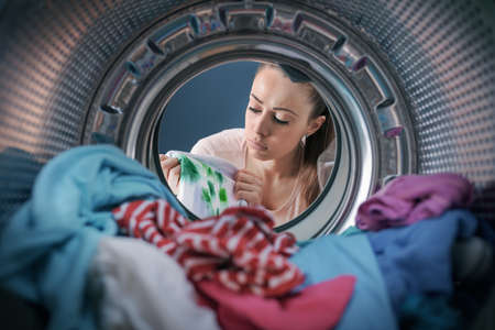 Disappointed woman finds stained clothes in the washing machine after doing laundry, point of view shotの写真素材