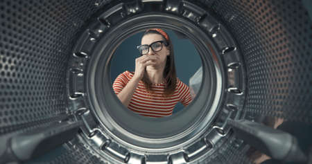 Disgusted woman looking into her smelly washing machine, she is holding her nose, point of view shotの写真素材