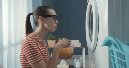 Woman waiting for the washing machine to finish: she is staring at the washing machine door and...