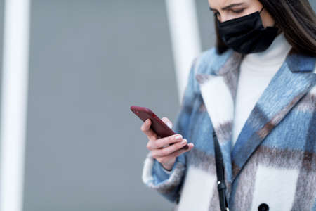 Woman with face mask spending time outdoors and using her smartphoneの写真素材