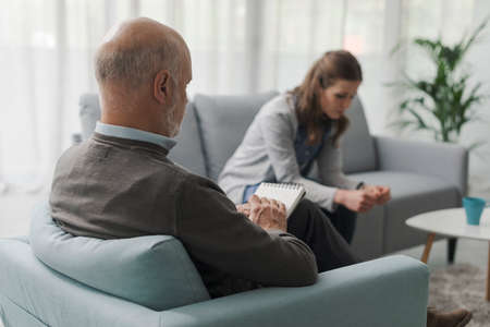 Depressed woman talking during a therapy session, the psychologist is writing notes and listeningの写真素材