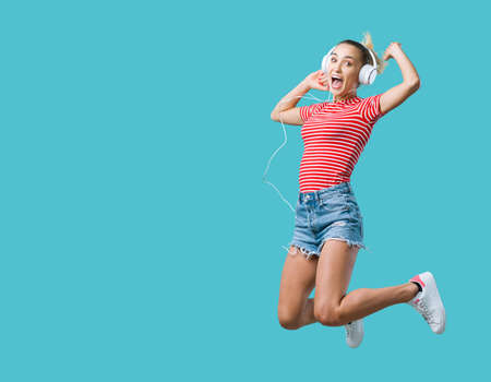 Cheerful young woman wearing headphones and listening to music, she is jumping and feeling excited
