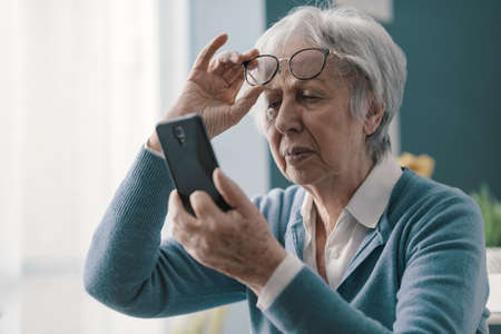 Senior woman having vision problems, she can't read the messages on her smartphone