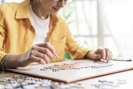 Woman sitting at desk at home and solving a puzzle, leisure and games conceptの写真素材