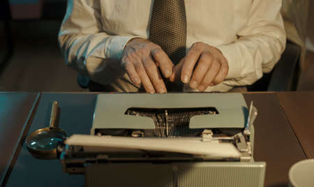 Vintage journalist working in the office: he is sitting at desk and typing on a typewriterの写真素材