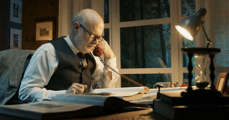 Academic professor sitting at desk and working, he receives a phone call