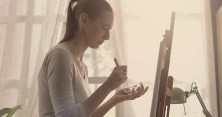 Female artist working in the atelier, she is painting on canvas using a spatula