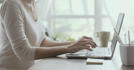 Businesswoman working from home, she is sitting at desk and typing on a laptop