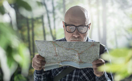 Worried tourist lost in the wilderness, he is checking a mapの写真素材