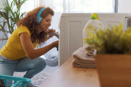 Happy young woman doing laundry at home, she is loading the washing machine and listening to musicの写真素材