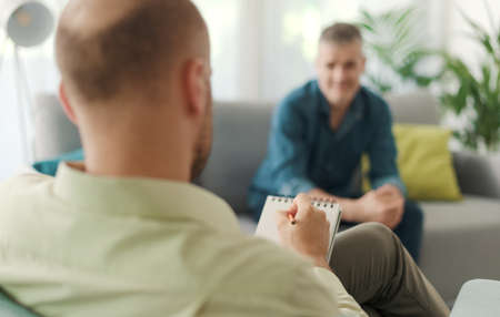 Professional therapist meeting a patient in his office, he is writing down notes and listeningの写真素材