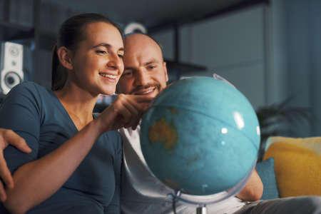 Happy couple picking a destination on the globe for their next travelの写真素材