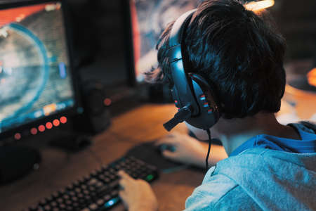 Young gamer wearing a headset and playing online multiplayer video games on his computer, entertainment and leisure conceptの写真素材