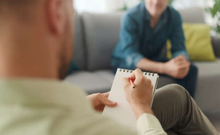 Professional therapist meeting a patient in his office, he is writing down notes and listeningの写真素材